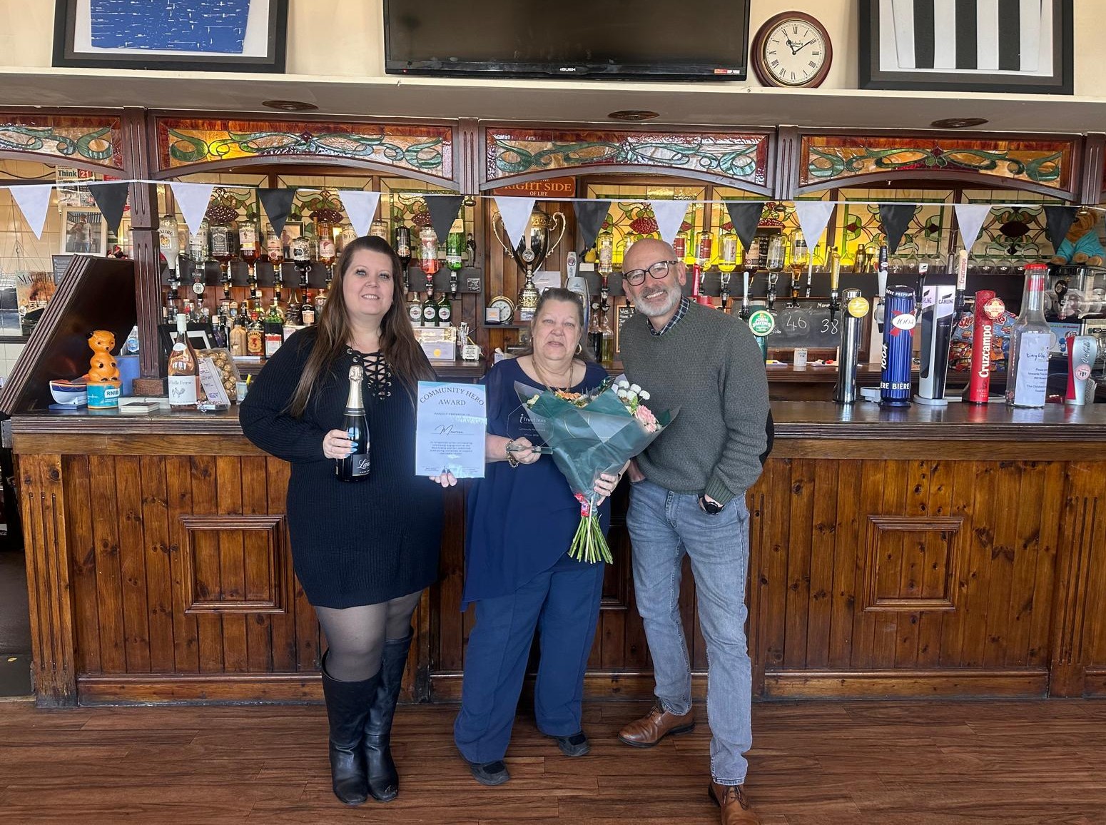 Community Hero of the Month award presentation at The Mauretania pub with staff holding certificate and flowers